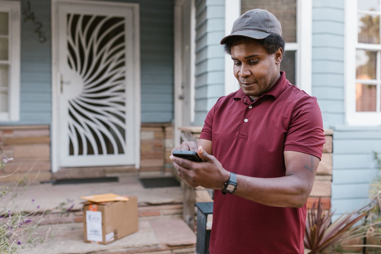 A man checking his phone beside a parcel on a doorstep.