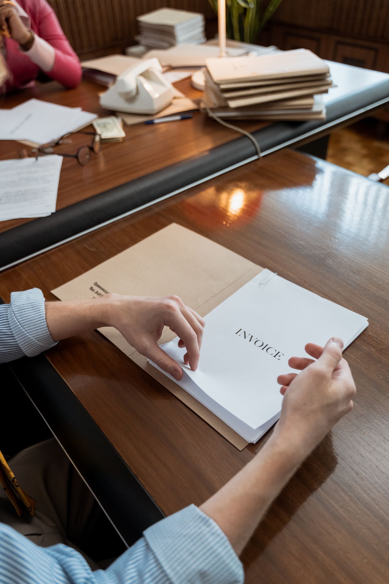 A hand arranging an invoice document on an office desk.