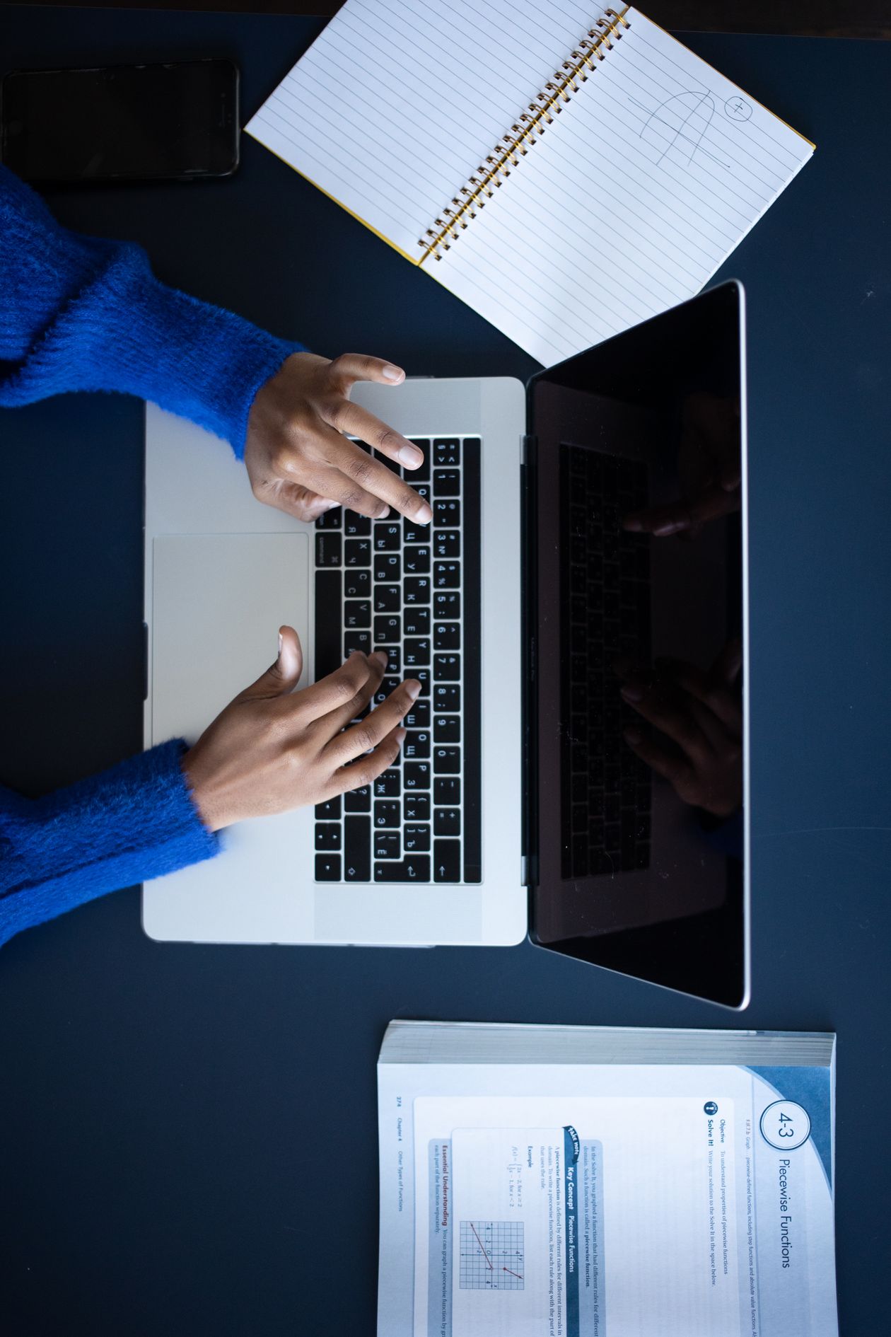 A person typing on a laptop keyboard at a desk.