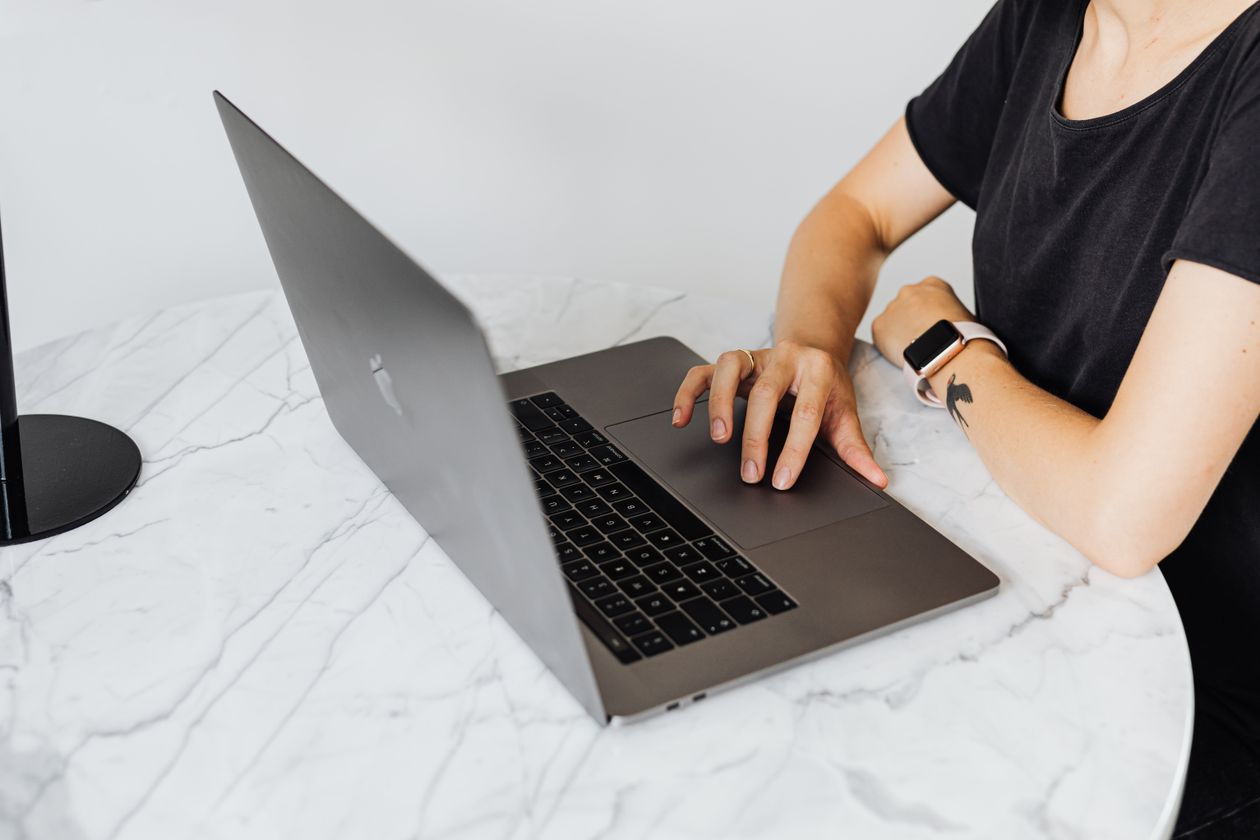 A person typing on a laptop trackpad at a marble table, wearing a smartwatch.