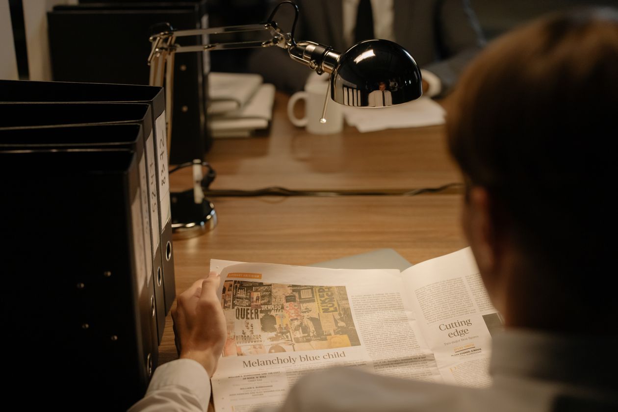 A person reading printed material at a desk under a lamp.