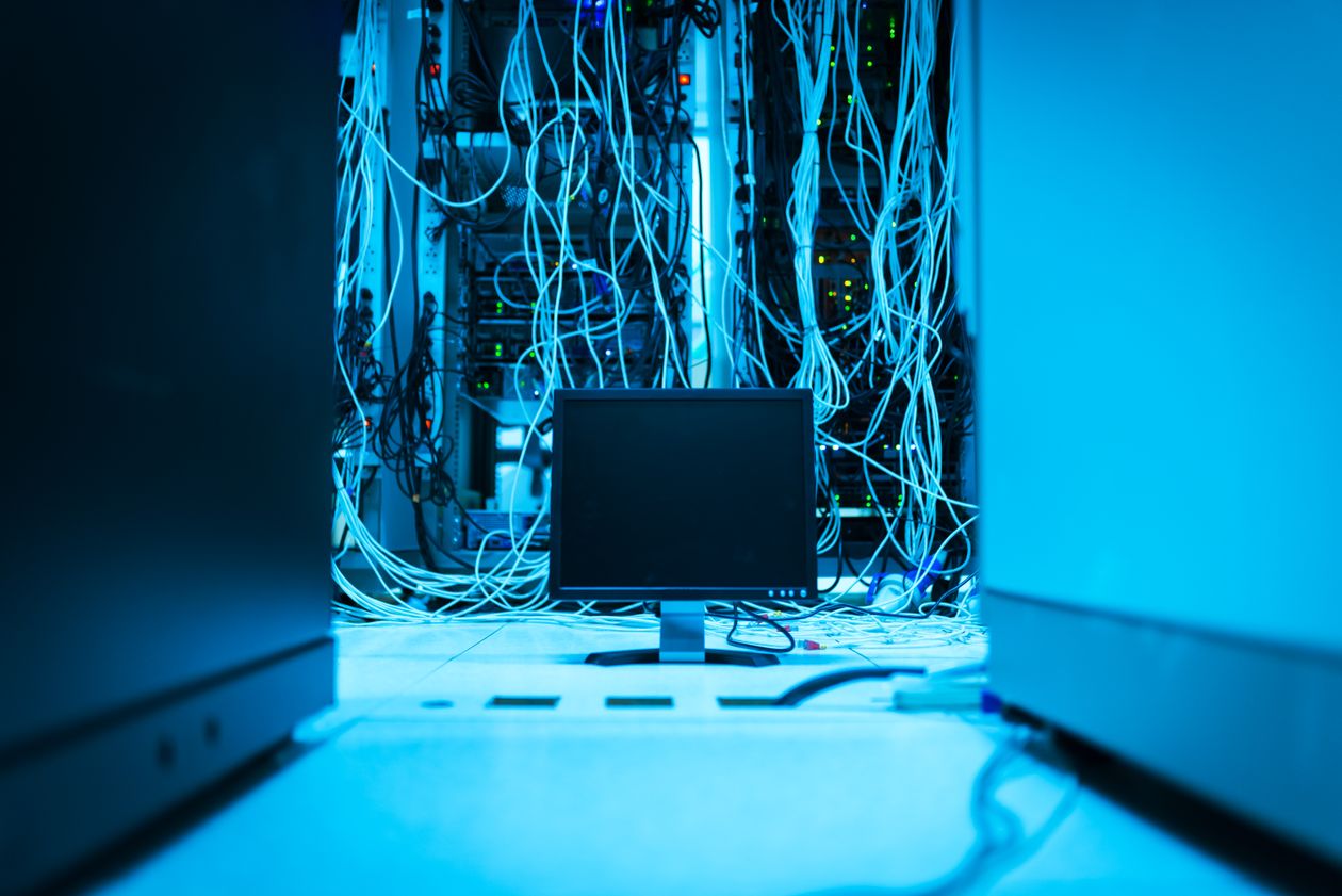 A darkened server room with a monitor and tangled network cables.