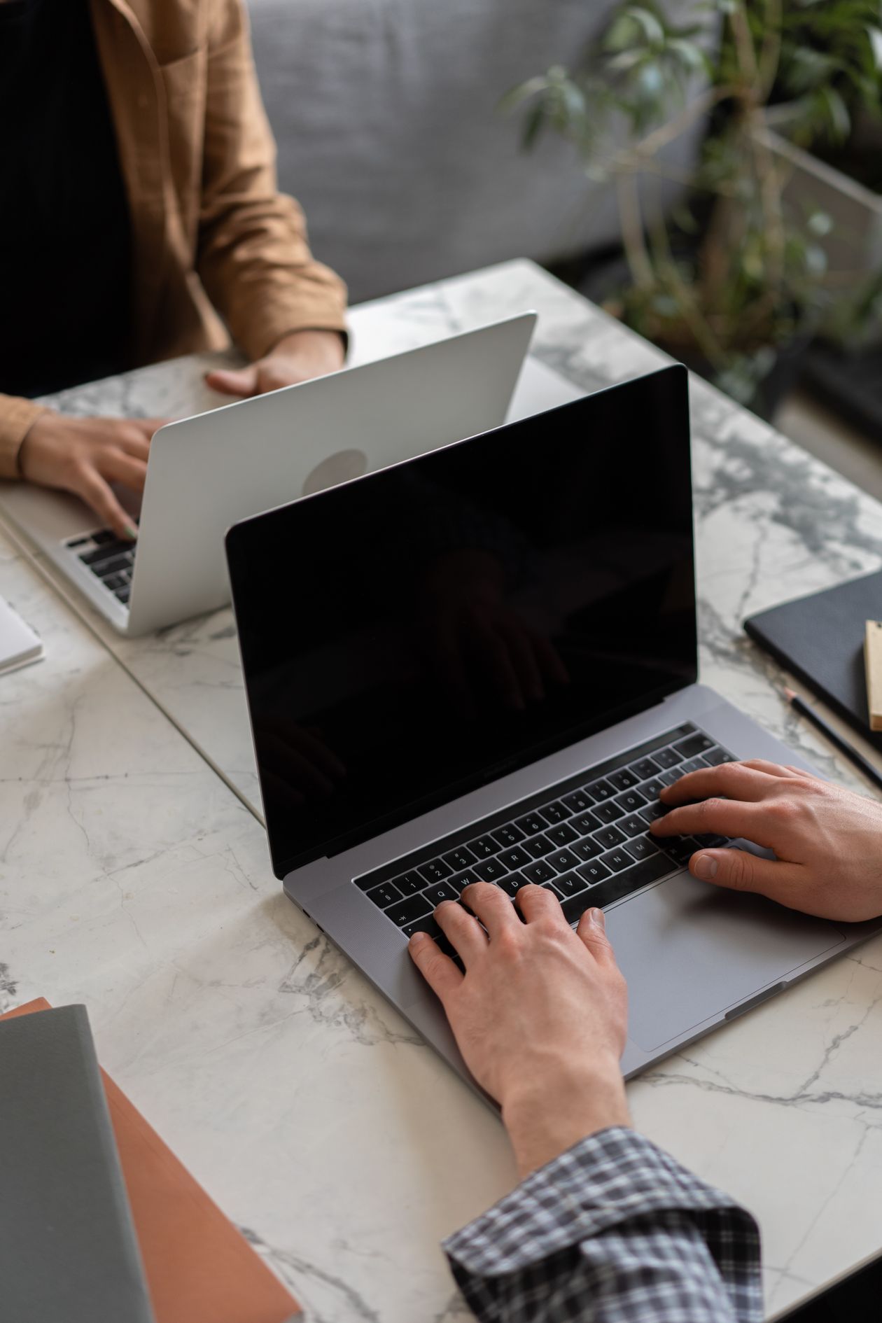 Two people working on laptops at a marble table.