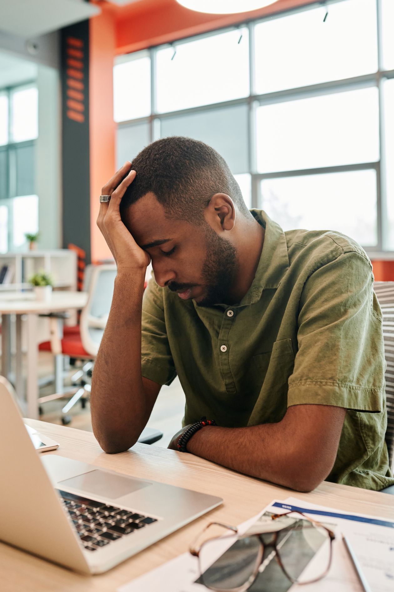 A man sitting at a desk with his head in his hand, laptop open in front of him.